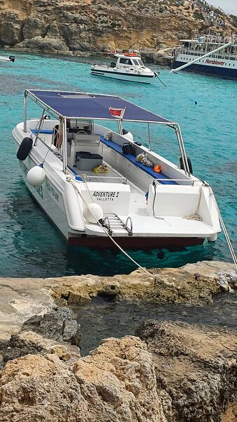 Adventure Cruises boat at anchor in clear water off Sliema.