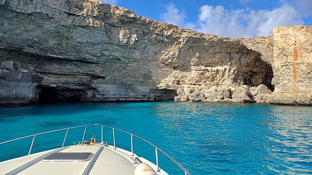 Powerboat bow approaching a Comino sea cave in turquoise water.