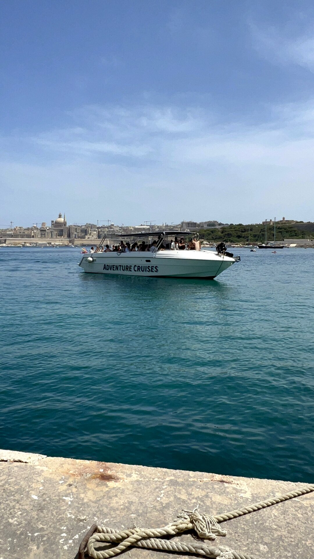 Adventure Cruises Malta powerboat with passengers, returning to Sliema Ferries with the Valletta skyline behind.
